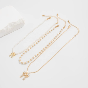 Detailed view of 3-piece layered necklace set with bow charms and faux pearls