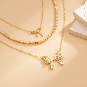 Detailed view of triple-layered gold necklaces with bow pendants and round bead chains