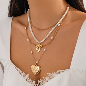 Detail of layered gold necklace with bow pendant, pearls, and heart locket with rose engraving
