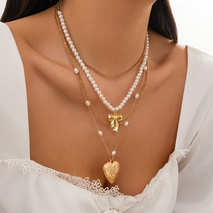 Close-up of layered necklace set with gold bow, faux pearls and heart locket pendant