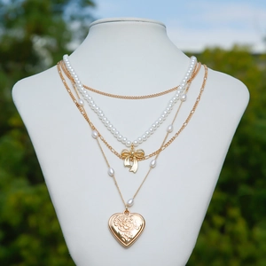 Detail view of multi-layered gold necklace with bow pendant, pearls and heart locket charm