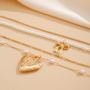 Close-up of layered pearl necklace featuring a golden bow and engraved heart locket