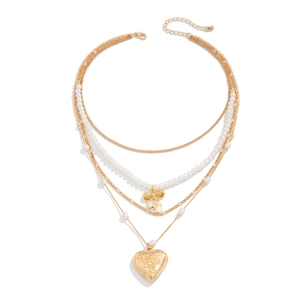 Detail of layered gold necklace featuring pearl strands, bow accent and rose heart locket