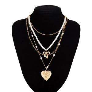 Detail of layered gold necklace with bow charm, pearls, and heart rose pendant