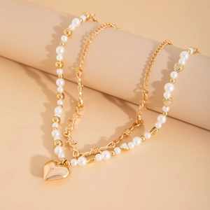Macro detail of a double-layered necklace with a gold heart pendant and faux pearls