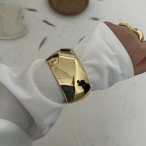 Close-up of polished gold wide geometric twisted cuff bracelet styled over white sleeve