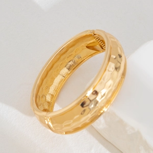 Detail of wide gold cuff bracelet featuring a hammered texture and hinge clasp design