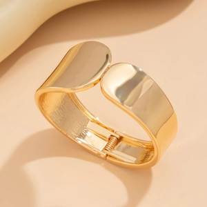 Primer plano de un brazalete ancho de metal dorado con cierre de bisagra y acabado pulido