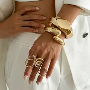 Brazalete dorado de ondas irregulares y anillos abstractos en modelo con ropa blanca