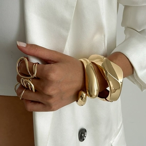 Conjunto de brazalete y anillos de metal dorado con diseño de ondas en blazer blanco