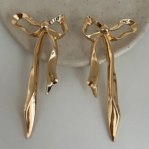 Detailed close-up of golden metallic bow-shaped drop earrings on a ceramic dish