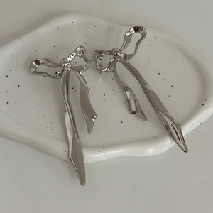 Detailed macro view of silver bow-shaped earrings with liquid metal texture on art tray