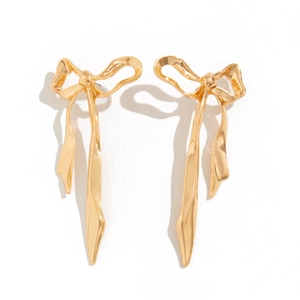 Macro shot of gold ribbon bow earrings with reflective metallic texture and wavy details