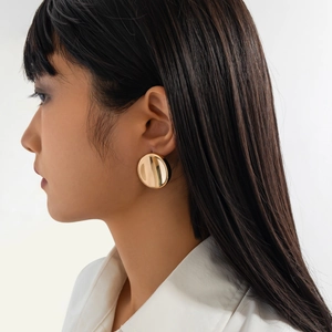 Close-up of a large polished gold circular stud earring worn by a model in lifestyle setting