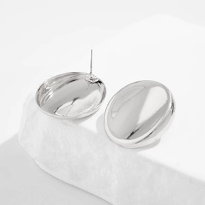 Detailed view of silver minimalist disk stud earrings on a white stone background