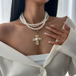 Three-layer faux pearl necklace with a large golden baroque cross pendant on a white suit