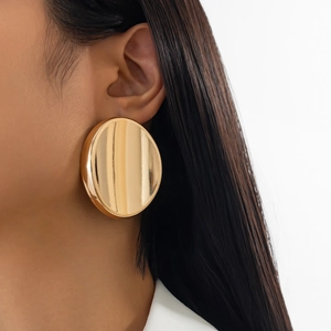 Close-up of large round gold mirror finish stud earrings worn by a model in minimalist style