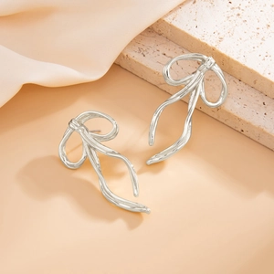 Macro detail of glossy silver ribbon bow earring on a textured stone and beige silk
