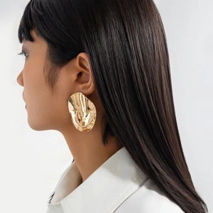 Detailed shot of large golden irregular wave texture earrings on model