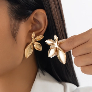 Macro detail of large gold leaf stud earrings with polished metallic petal texture