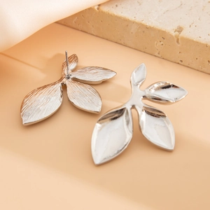 Detailed macro view of silver triple-leaf petal earrings on elegant silk fabric