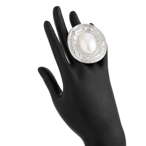 Dettaglio dell'anello oversize in metallo liquido argento con perla ovale su mano nera