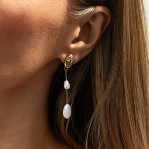 Dettaglio di orecchini dorati irregolari con perle barocche eleganti su una modella