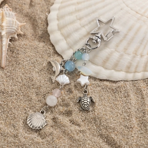 Marine themed keychain with dolphin and turtle charms on beach sand with sea shells