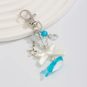 Macro detail of blue whale keychain with white bow and star charms on white display