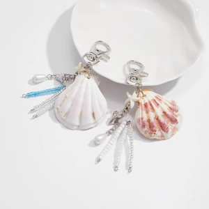 Detail of seashell keychain with starfish charm and blue beads on white ceramic tray