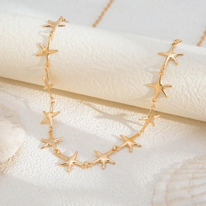 Detailed view of golden starfish waist chain draped over white sandy textured props