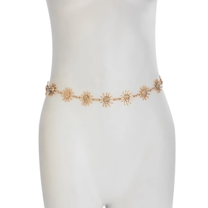 Macro shot of gold sun face charms and link chain on a white mannequin waist
