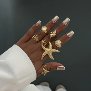 Nahaufnahme von goldenen Seestern- und Muschelringen im Meeresstil an einer Hand