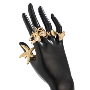 Detailansicht goldener Seestern- und Muschelarmreifen an einem Handmodell mit Mattfinish