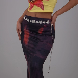 Détail d'une chaîne de taille fleurie en métal argenté avec une jupe tie-dye vintage