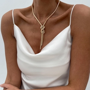 Close-up of golden flat snake chain necklace featuring a decorative knot and tassel detail
