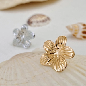 Detailansicht goldener und silberner Blumenohrringe mit Textur auf einer Muschelunterlage