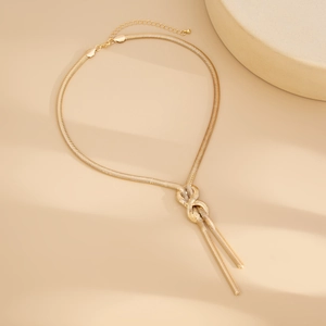 Detail of gold snake chain necklace featuring a unique tie-knot design and tassel pendants
