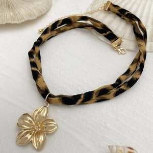 Detailed shot of leopard print fabric choker with large gold floral pendant on white shell