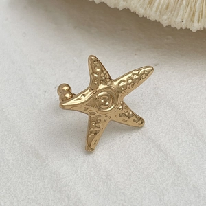 Nahaufnahme der goldenen Seestern-Ohrklemme mit Texturdetails auf weißer Koralle