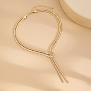 Detail of gold layered snake chain necklace featuring a minimalist metal knot and tassel