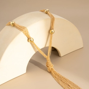 Detail of layered gold snake chain necklace with polished beads and tassel knot
