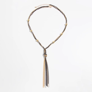 Macro detail of layered metallic snake chains with gold beads and tassel knot design