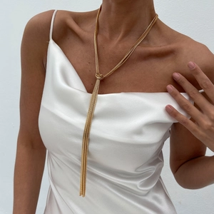 Detail of a long gold knotted tassel necklace with multi-layer chains on a white dress