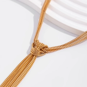 Macro detail of multilayer golden box chain necklace with a decorative knot and tassel