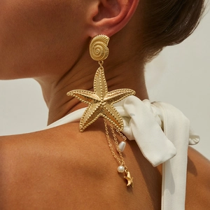 Detailaufnahme goldener Seestern-Ohrring mit Perlenquasten auf weißem Grund