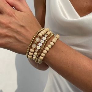 Detail of bohemian layered bracelets set featuring wood beads and golden MAMA letter charms