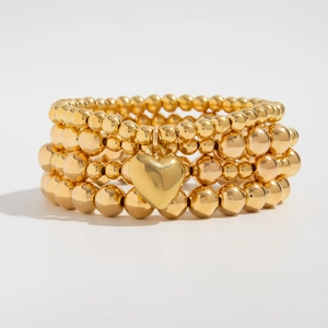 Detailed close-up of four-piece stackable gold beaded bracelets with heart charm