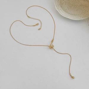 Flat lay of a gold snake chain necklace shaped like a heart with a unique knotted pendant