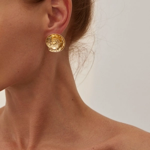 Close-up of golden spiral lava earrings with hammered texture on female model ear